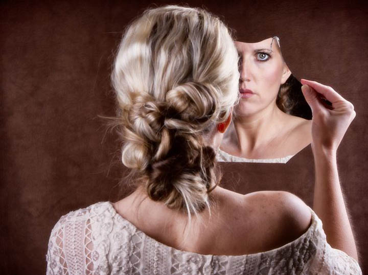 Woman looking into a broken mirror representing her low self-esteem. 