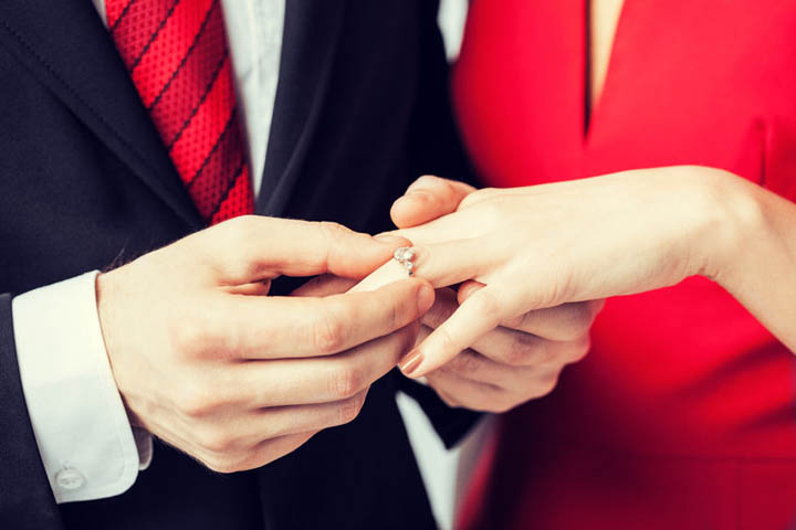 Picture of man putting wedding ring on woman hand signaling engagement.