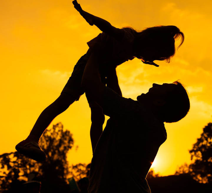 Silhouette of a father and daughter who play outdoors at sunset background.