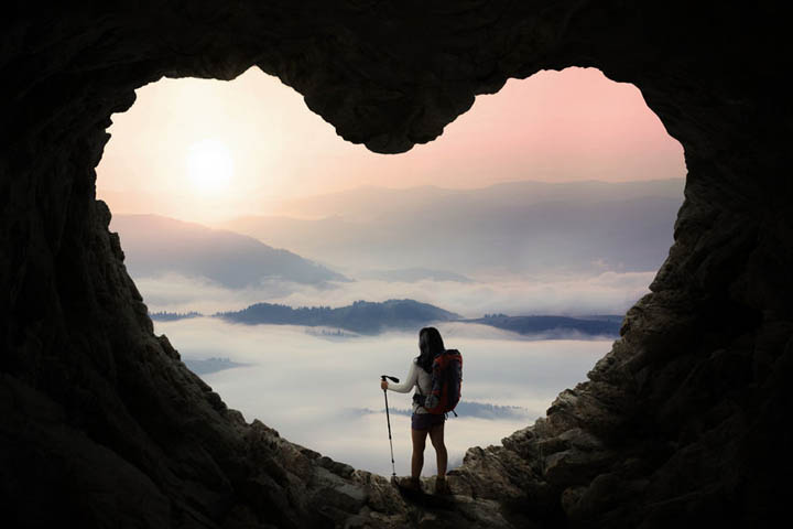 A woman hiking through a heart shaped cave symbolizing going through heartbreak.