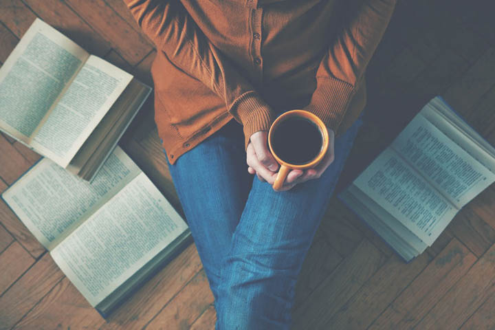 Woman having a cup of coffee surrounded by books representing her story.