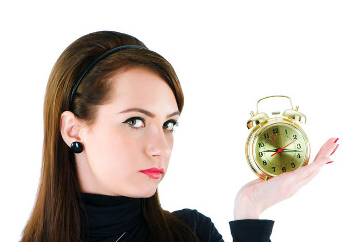 A beautiful woman looking pensive holds a clock wondering if she is wasting her time with her boyfriend.