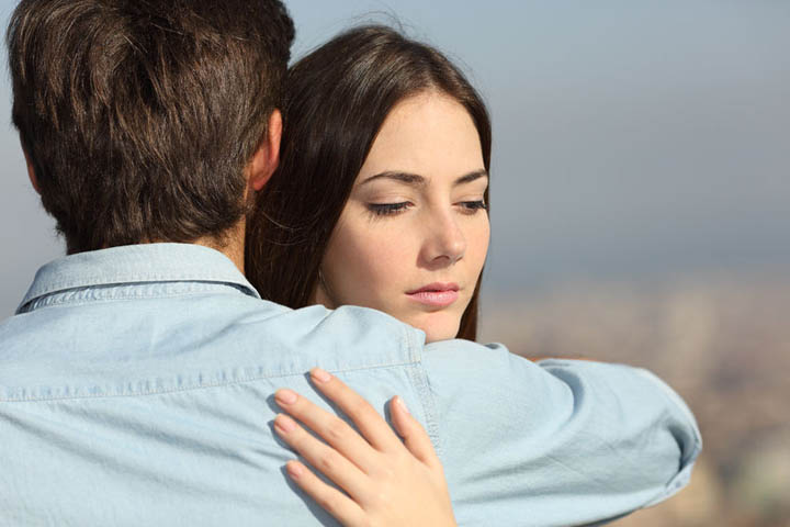 Sad woman hugging her emotionally unavailable boyfriend and looking down.