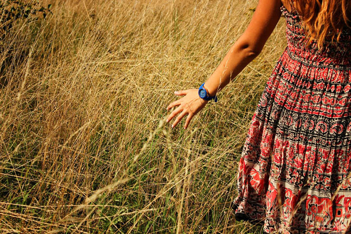 Beautiful woman walking in the field and runs hand through the high dry grass in autumn.