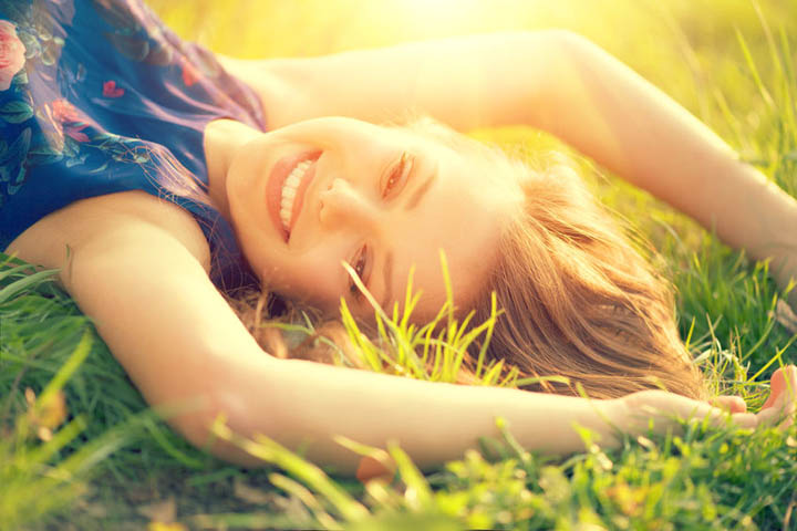 Beautiful, happy, smiling woman lying on the field in green grass.