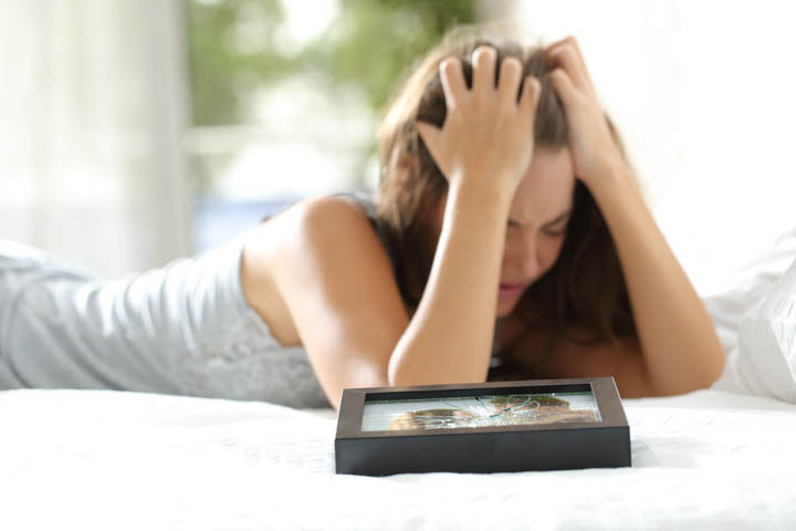 Sad woman missing her boyfriend after breakup with a broken picture of the couple on the bed.
