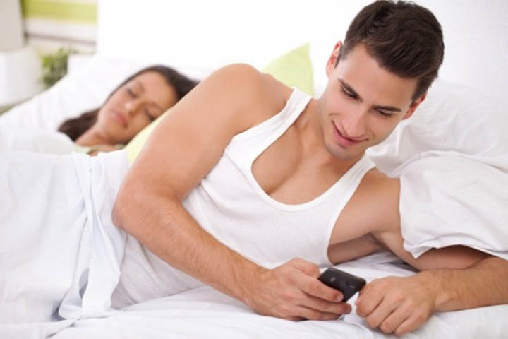 Man is cheating on his girlfriend texting the other woman while she sleeps in bed next to him.