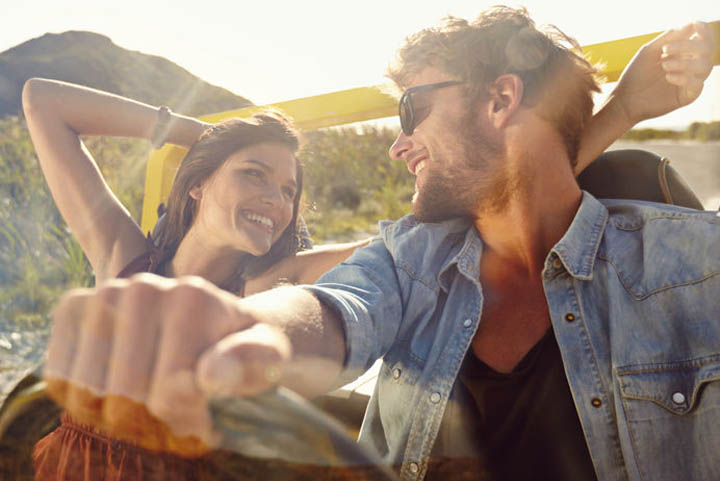 Happy young man and woman in a car enjoying a road trip on a summer day. Couple out on a drive in a open car.