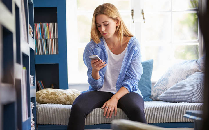 A beautiful woman is sitting On Couch At Home anxiously looking at her phone wondering why he hasn't responded.