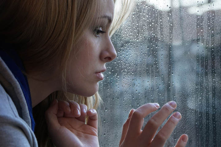 Beautiful woman looking out the window on a rainy day, wondering if it serves her.