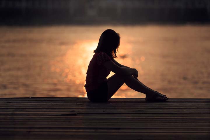 Silhouette of sad woman looking at sunset over water, shame concept