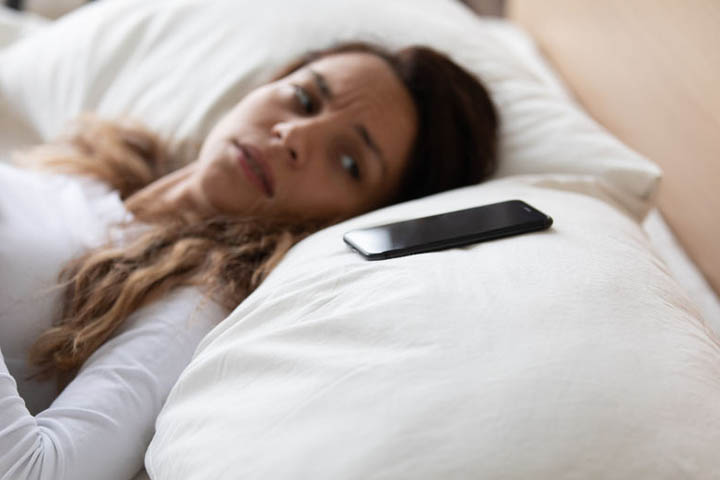 An anxious woman lying in bed is looking at her phone wondering why she hasn't heard from him in days.