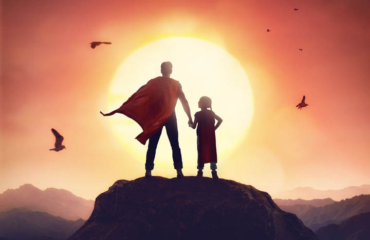Father and daughter playing outdoors in superhero costumes, on top of mountain looking in sunset