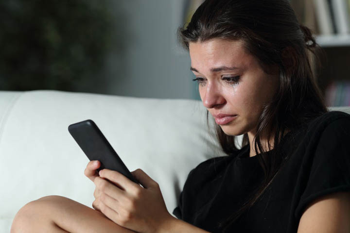 Sad beautiful woman checking phone after boyfriend broke up with her over text.