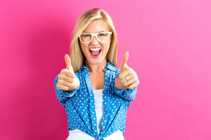 happy young woman giving thumbs up on a pink background