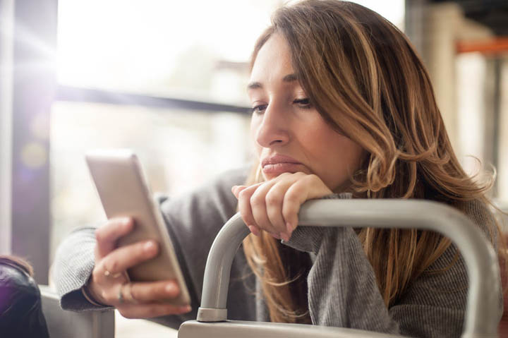 Woman sad over breakup looking at mobile phone on the city bus wondering why he doesn't love her